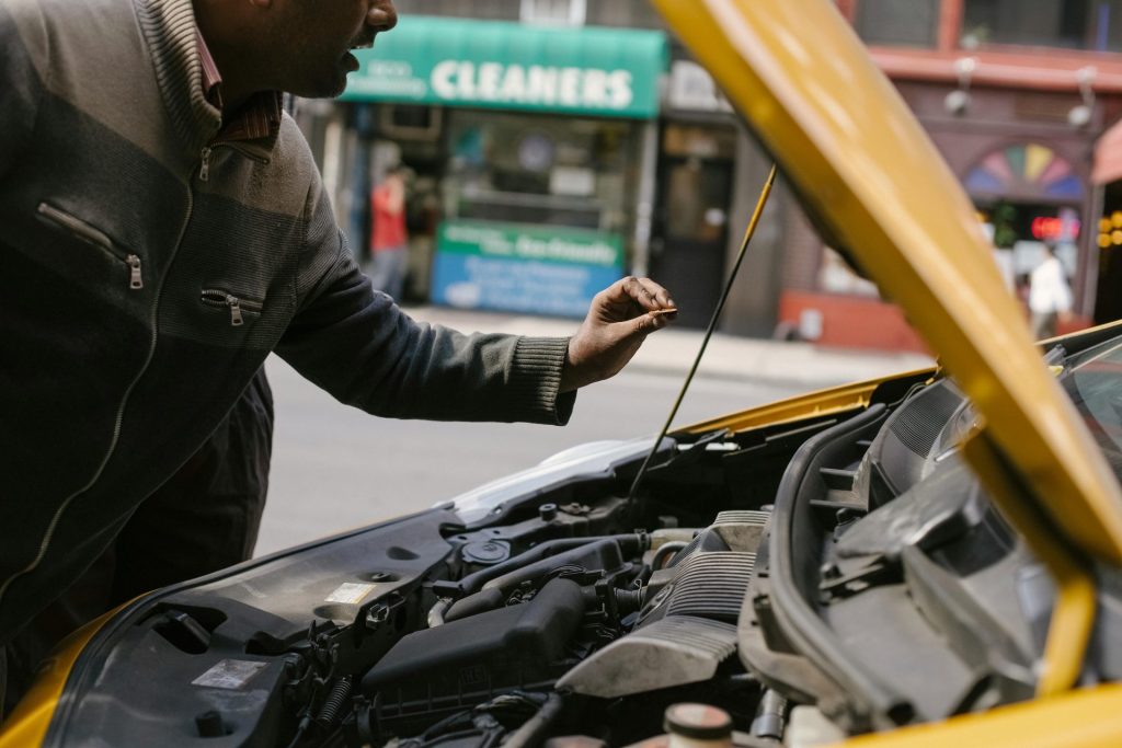 Mechanic examining car engine on a city street, highlighting vehicle maintenance.